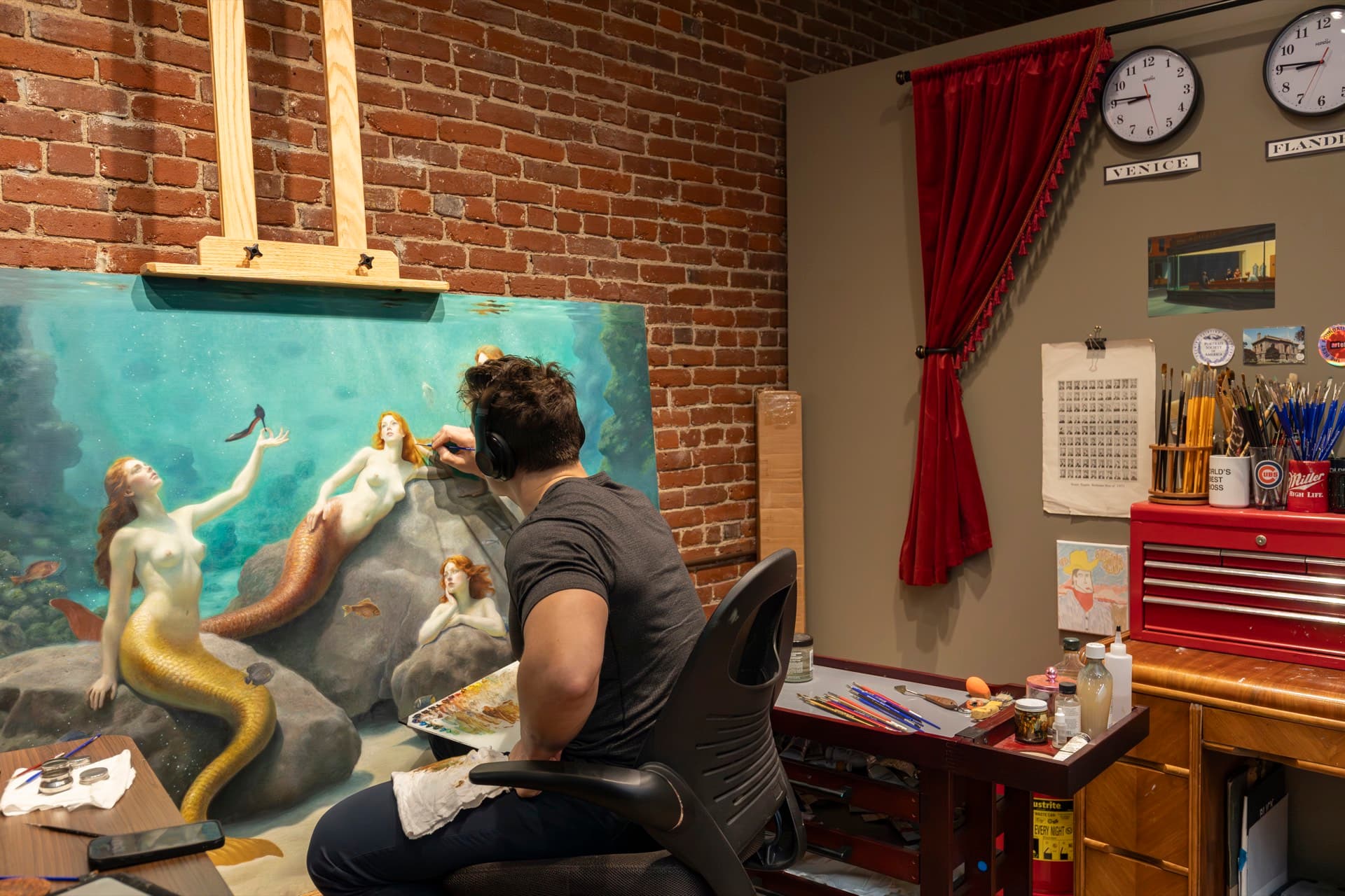 A fellow painting a large figure composition of mermaids at the easel in the studios