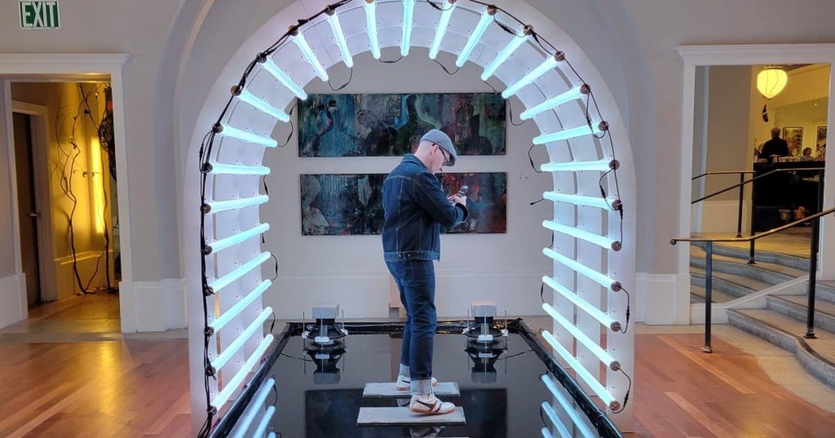 A visitor crossing the neon light walkway and reflecting pool at The Coliseum of Art