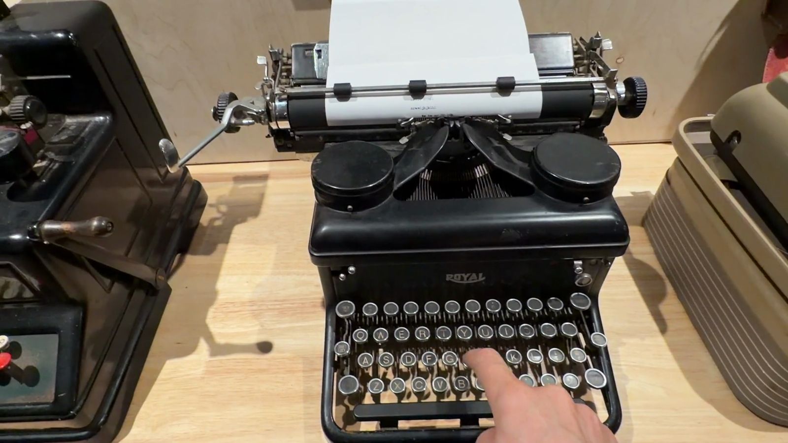 A hand on the keys of a black manual typewriter with paper loaded